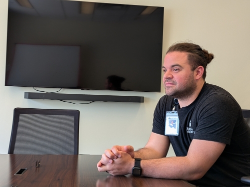 Man in a black shirt sits in a conference room.