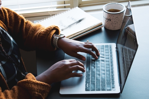 person typing on laptop next to coffee mug and notebook with pen