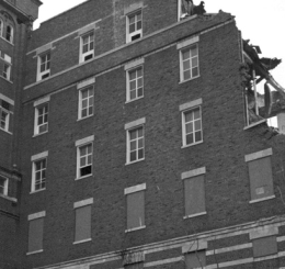 black and white photo of building being demolished by wrecking ball on crane