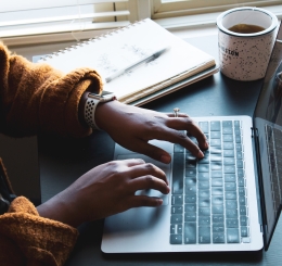 person typing on laptop next to coffee mug and notebook with pen