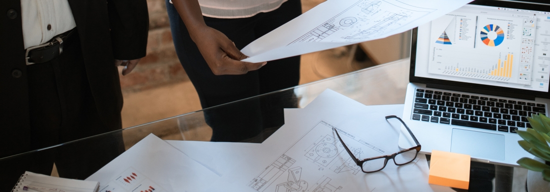 people standing near papers, glasses, and laptop on table