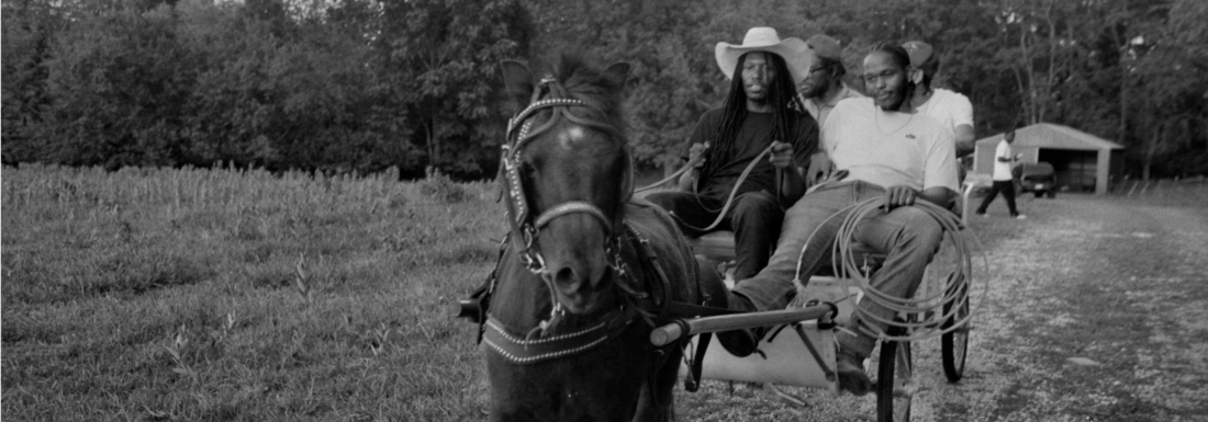 black and white image of 4 men on wagon pulled by horse