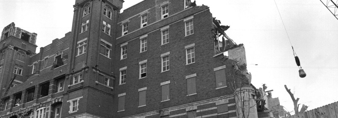 black and white photo of building being demolished by wrecking ball on crane