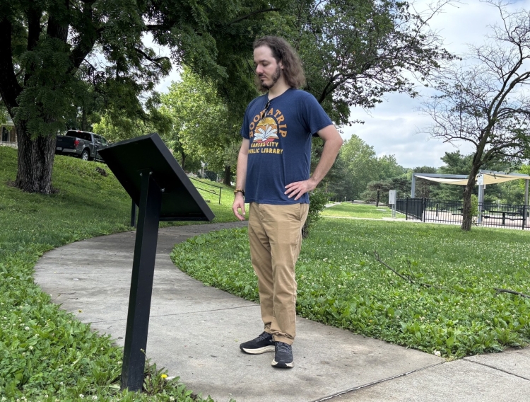 man looking at sign in park on sidewalk