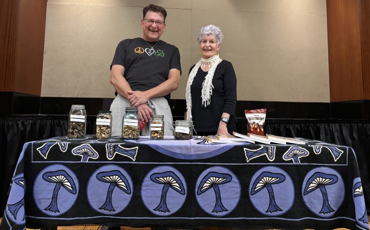 Mushroom experts Russ Davenport and Maxine Stone stand at a table with a mushroom tablecloth at the Library.
