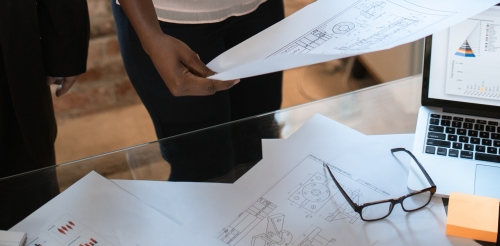 people standing near papers, glasses, and laptop on table