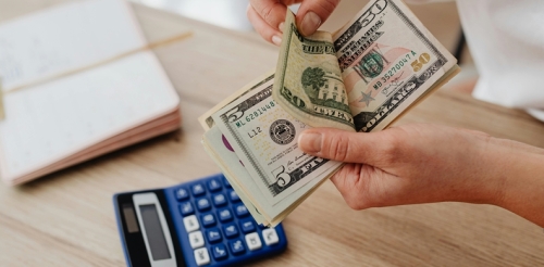 money in hands, calculator and clipped paper on table